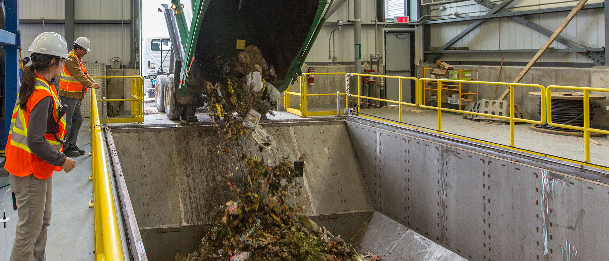 Two employees watch as a garbage truck delivers domestic and municipal waste.