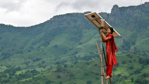 Woman on ladder installing solar panel above home.