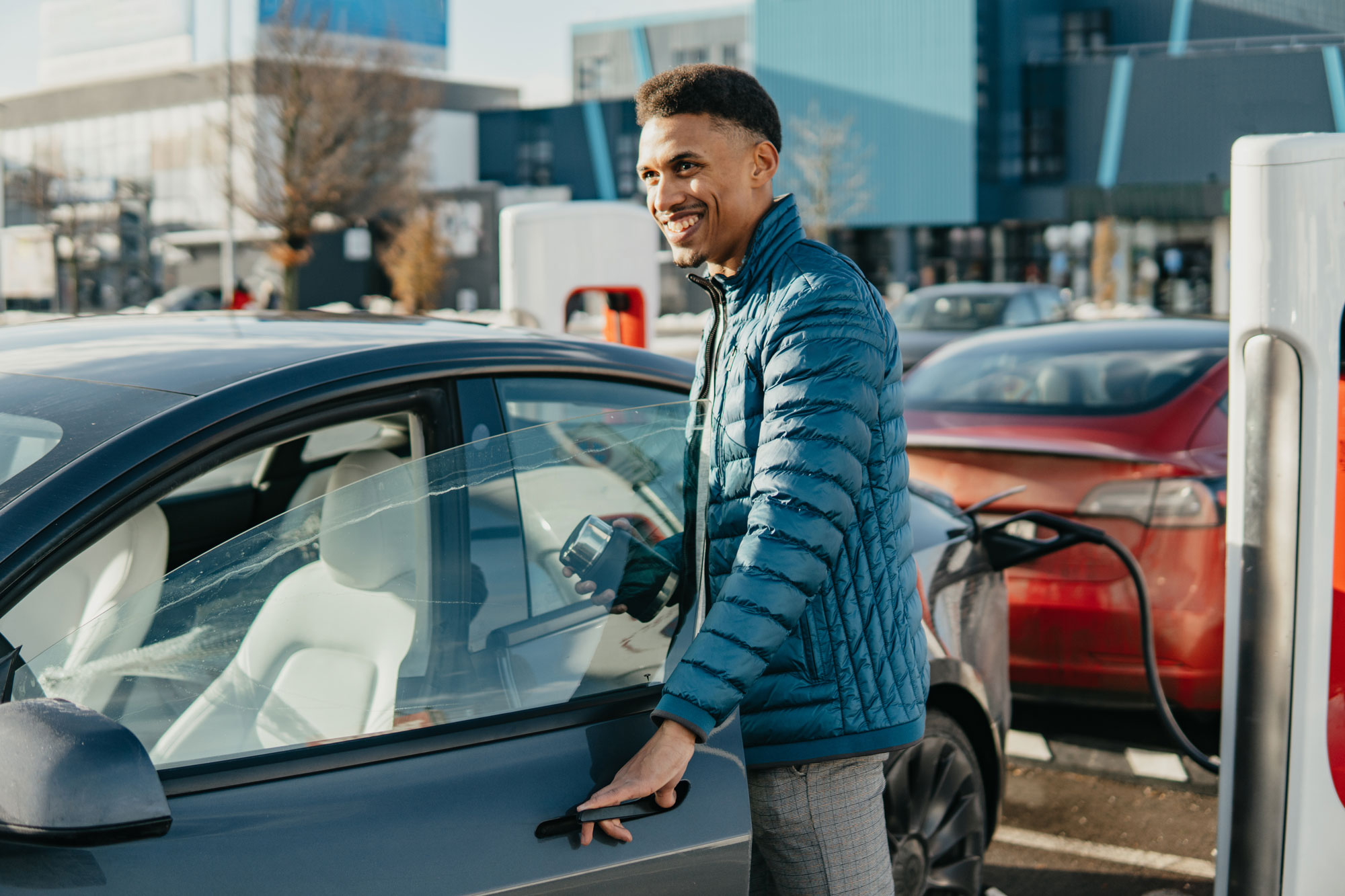 Man holds coffee mug while electric vehicle is charging.