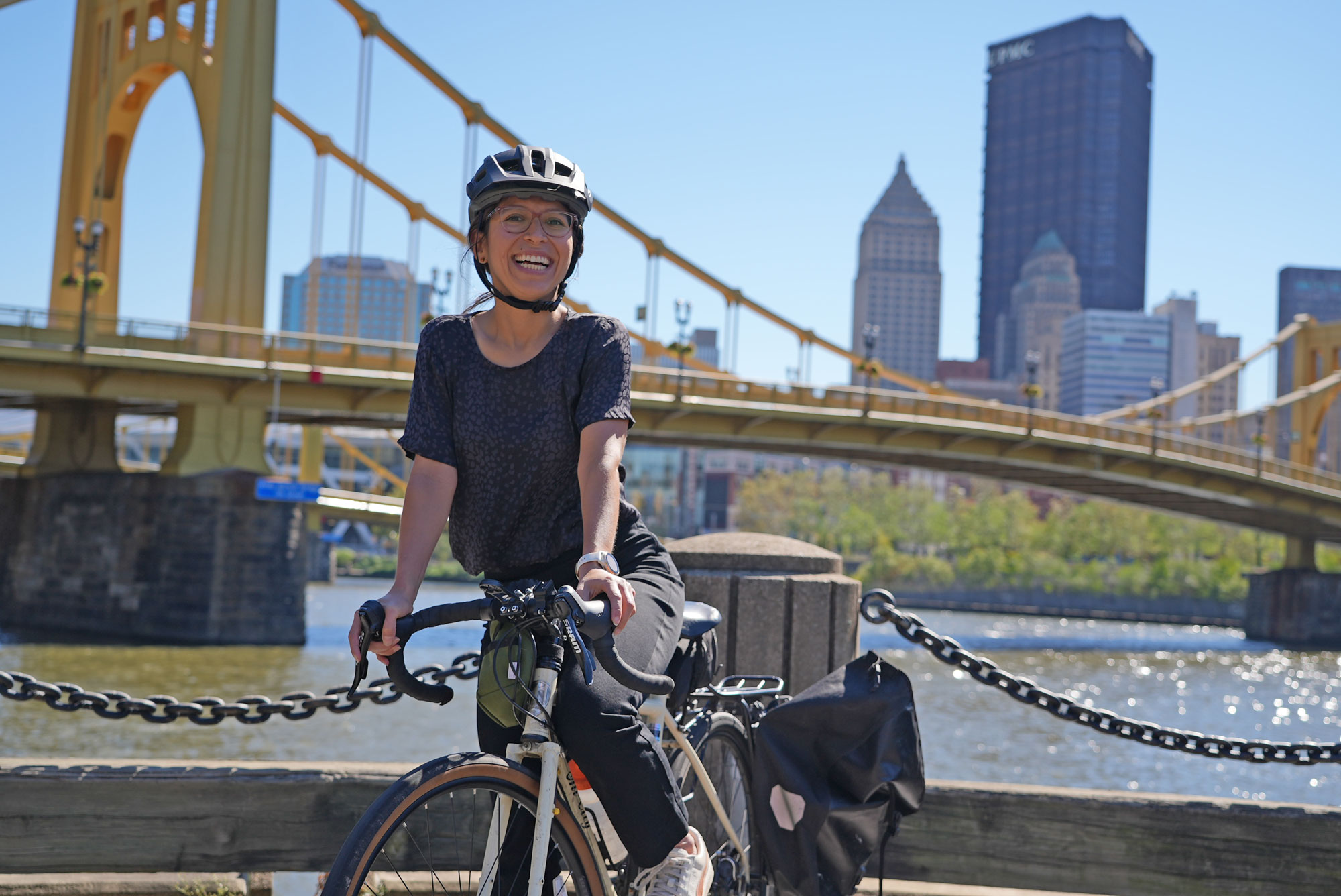 Angie Martinez seated on a bicycle in front of a bridge in Pittsburgh, Pennsylvania