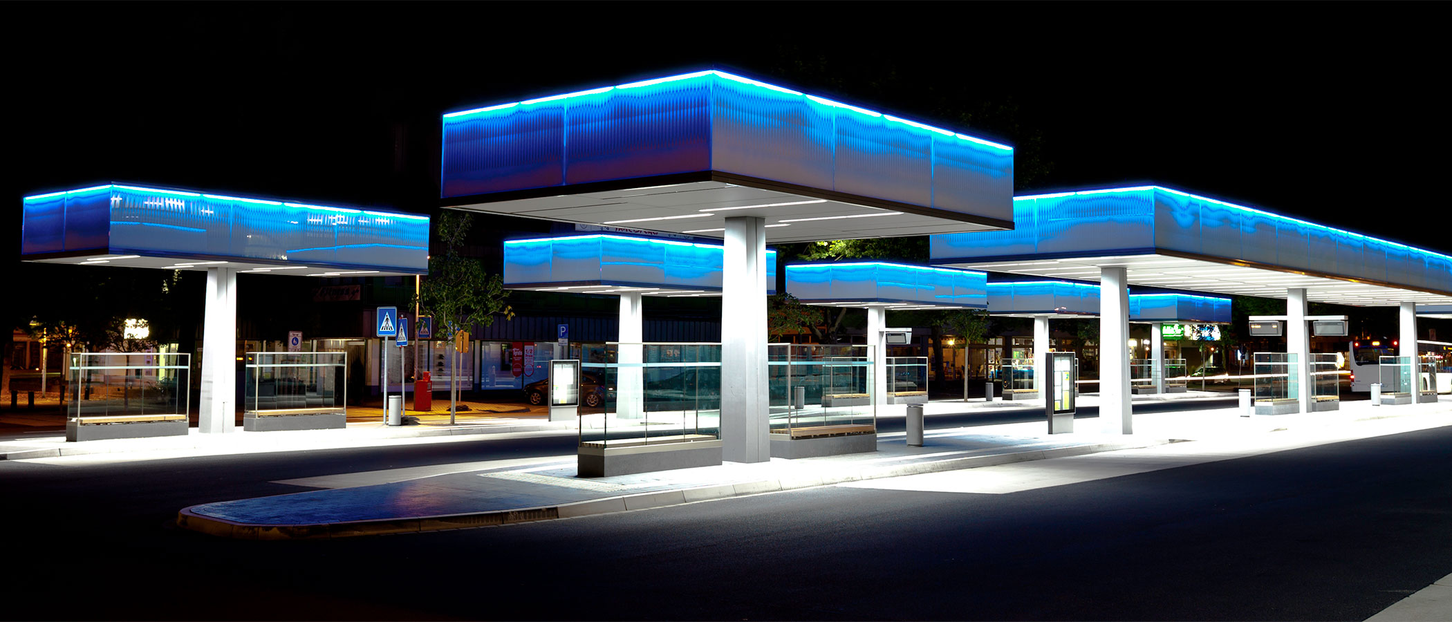 A modern bus terminal lit by blue and white LED lighting under protected canopies.
