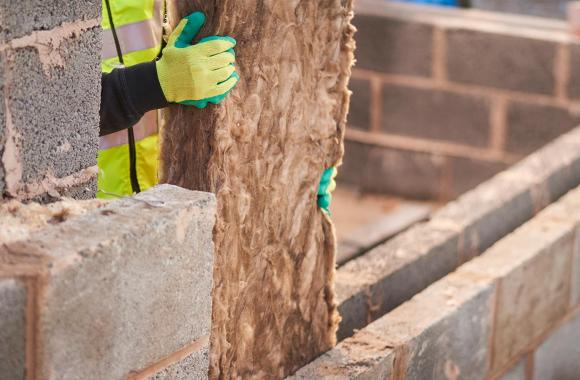 Worker installing cavity insulation between interior and exterior brick walls.